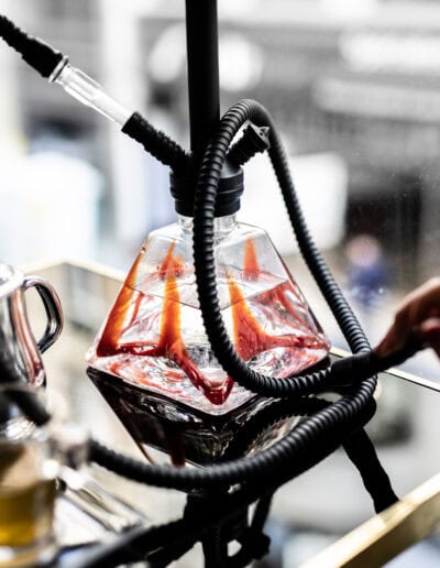 Une chicha moderne avec un design transparent et des tuyaux noirs, posée sur une table en verre avec des reflets lumineux.