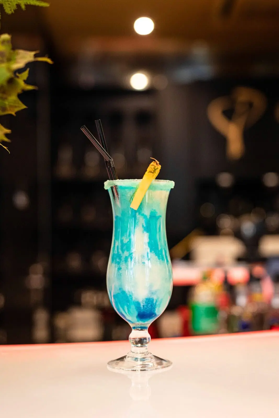 Cocktail bleu tropical avec garniture d'ananas Un cocktail bleu vif servi dans un verre tropical, garni d'une tranche d'ananas et de deux pailles noires.