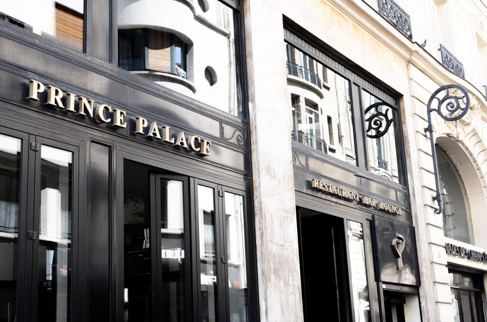 Façade d'un établissement nommé "Prince Palace" avec des inscriptions dorées indiquant "Restaurant Bar Lounge", située dans un bâtiment moderne avec des fenêtres en verre et des éléments architecturaux élégants.
